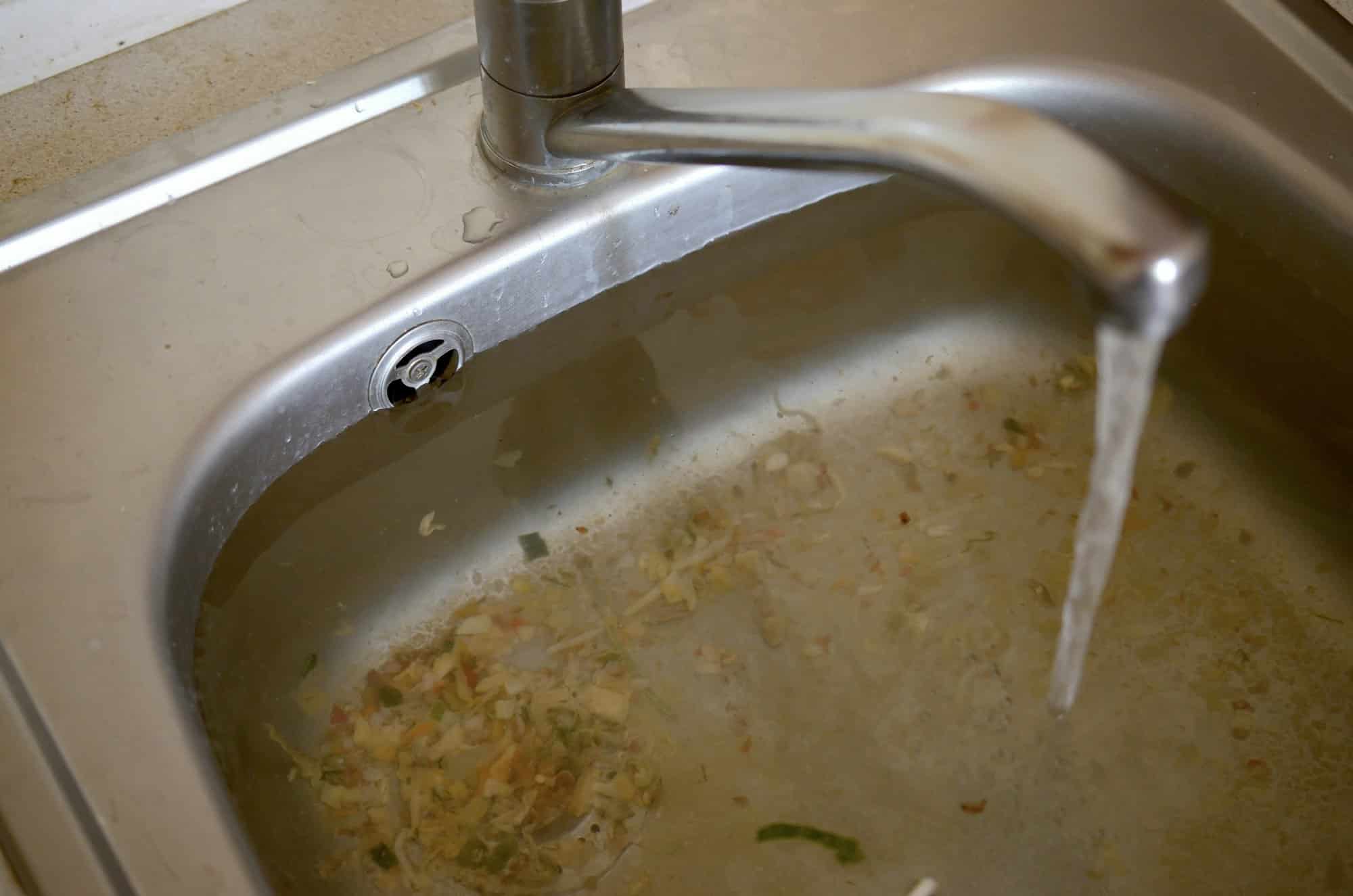 Stainless steel sink plug hole close up full of water and particles of food