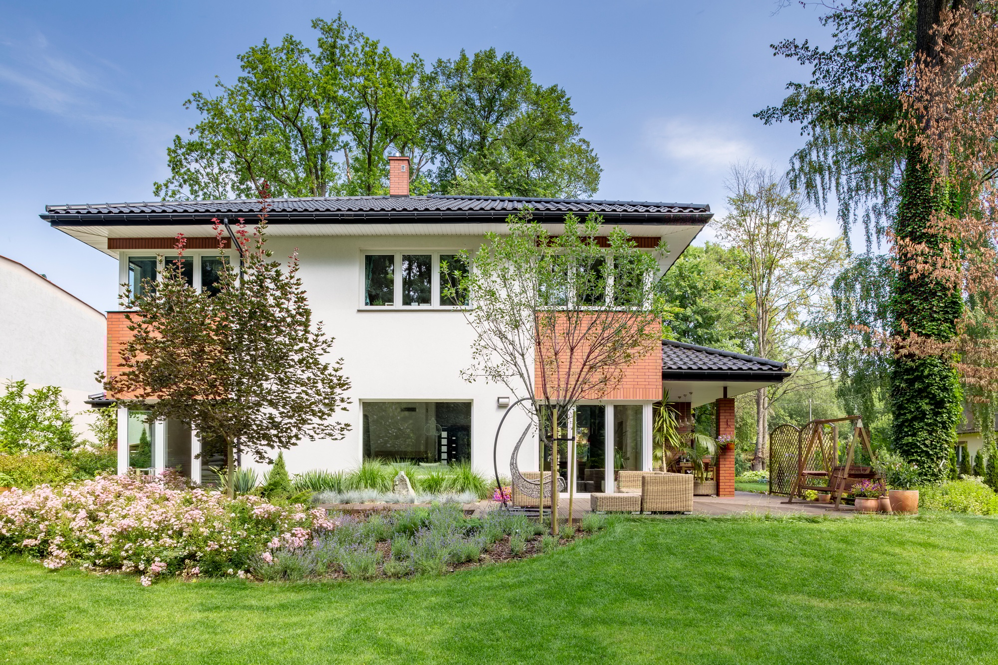 Flowers and trees in the garden of white house with windows duri